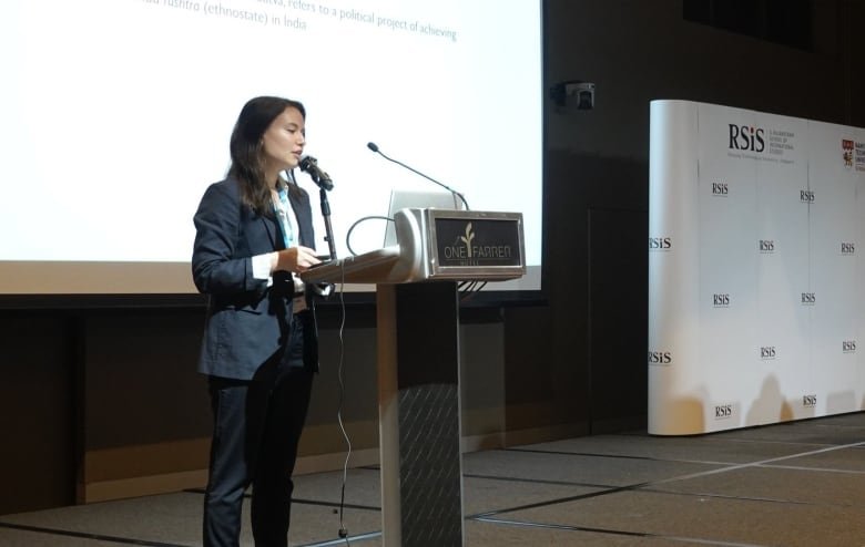 A woman in a suit speaks at a conference.