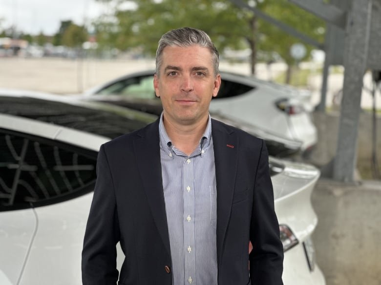 A man in a suit stands in front of a car.