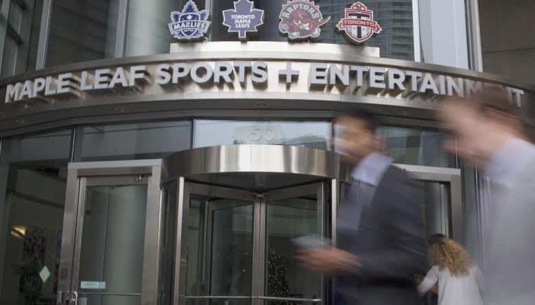 Two people in motion walk by a building with Maple Leaf Sports and Entertainment written across the entranceway.