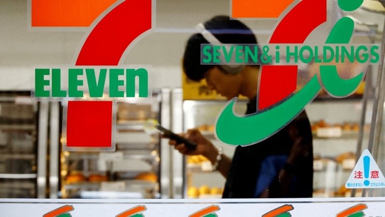 A person is seen unfocused through the window of a 7-Eleven.