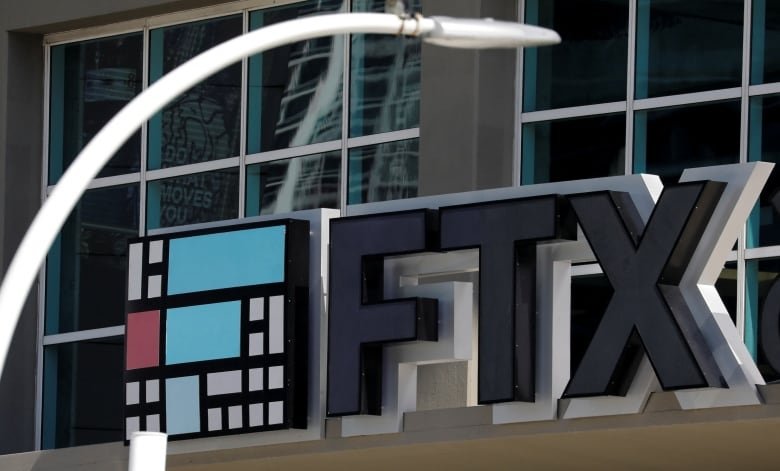 Big 3D black letters spell out FTX on the side of a building. A blurry white lamppost is visible in the image in front of the building facade.