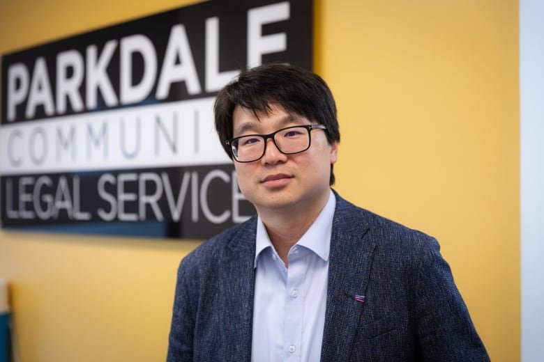 Lawyer John No stands in front of a sign for Parkdale Community Legal Services in the legal clinic’s office.