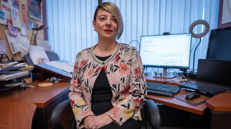 Woman sitting at a desk, looking directly at camera.