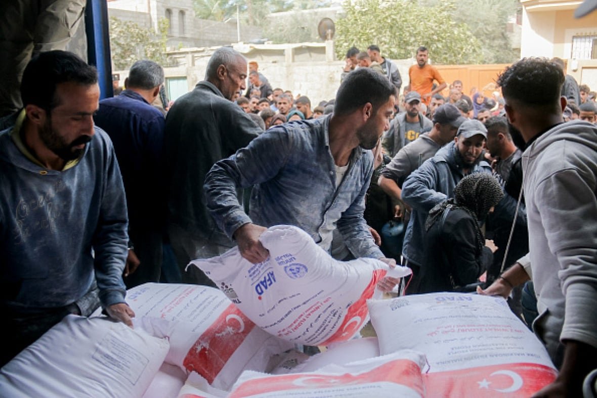 aid-and-gaza Men lift bags of food off a truck. A crowd of people surge behind them.