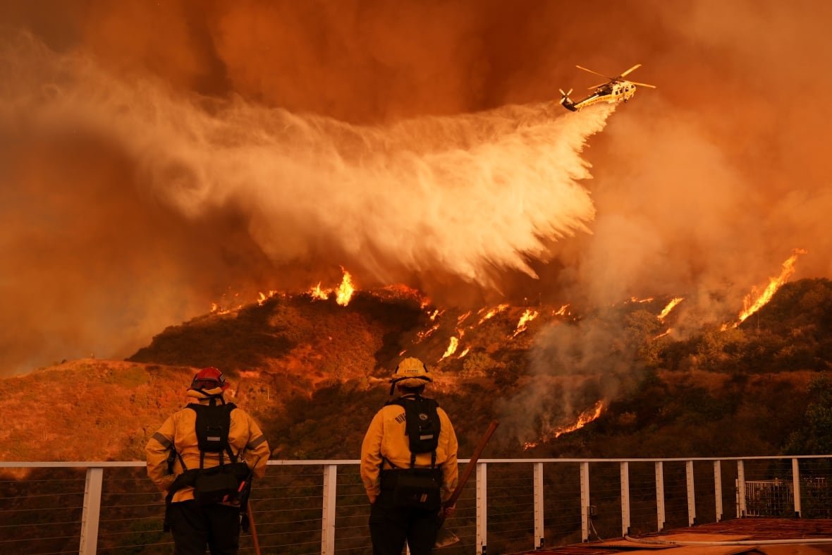 Firefighters watch on as a helicopter drops water over a wildfire.