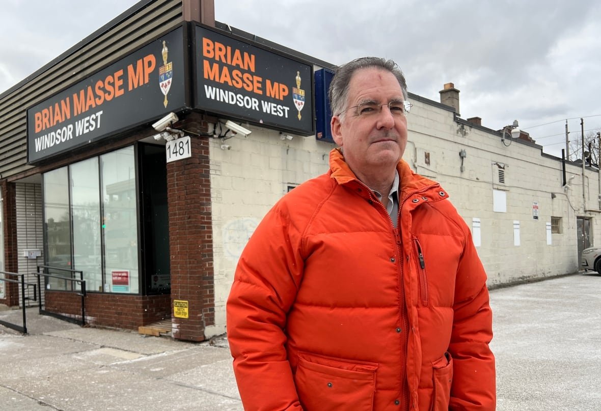 Man in orange jacket standing outside a building.