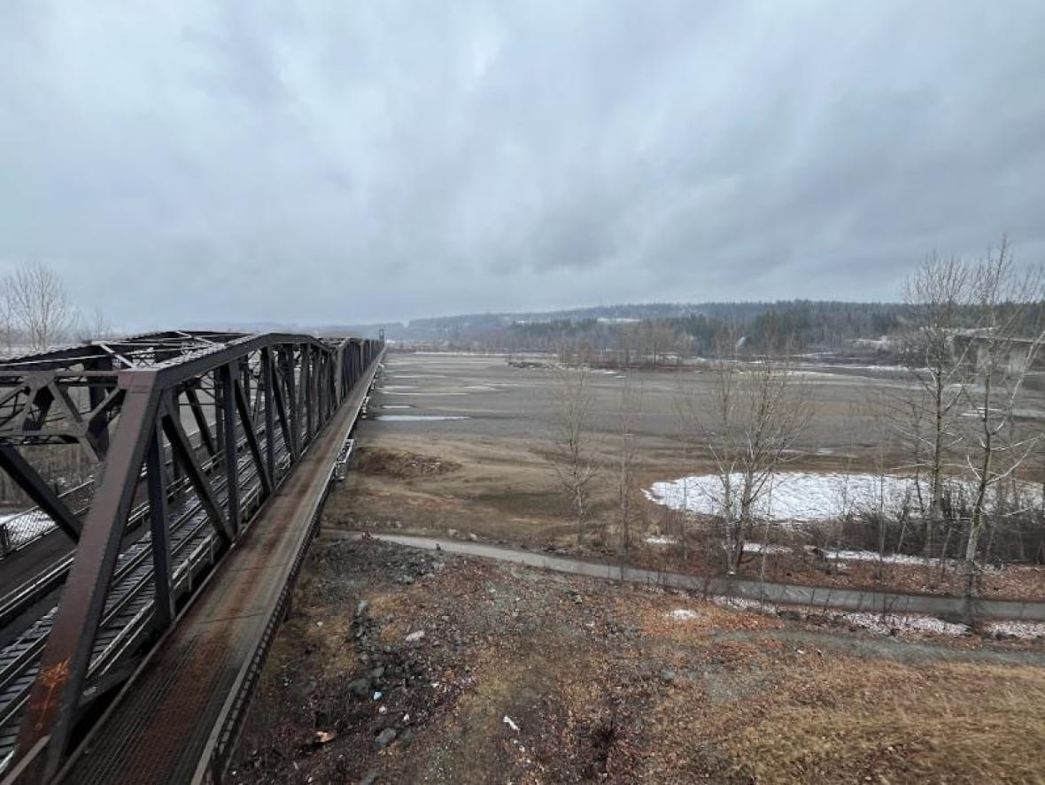 A train bridge spans a dry riverbed in a flat brown landscape.