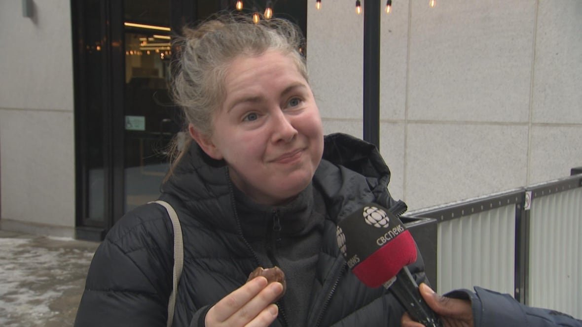 A woman holding a piece of chocolate tilts her head and makes a face.