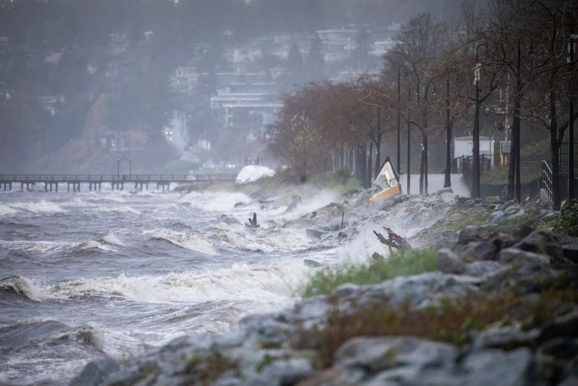 Big ocean waves hit rocks near a residential development.