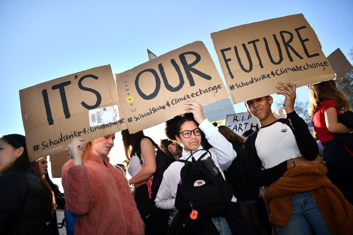 Young demonstrators hold cardboard signs that, when connected, say "It's out future" in black letters, along with several hashtags.