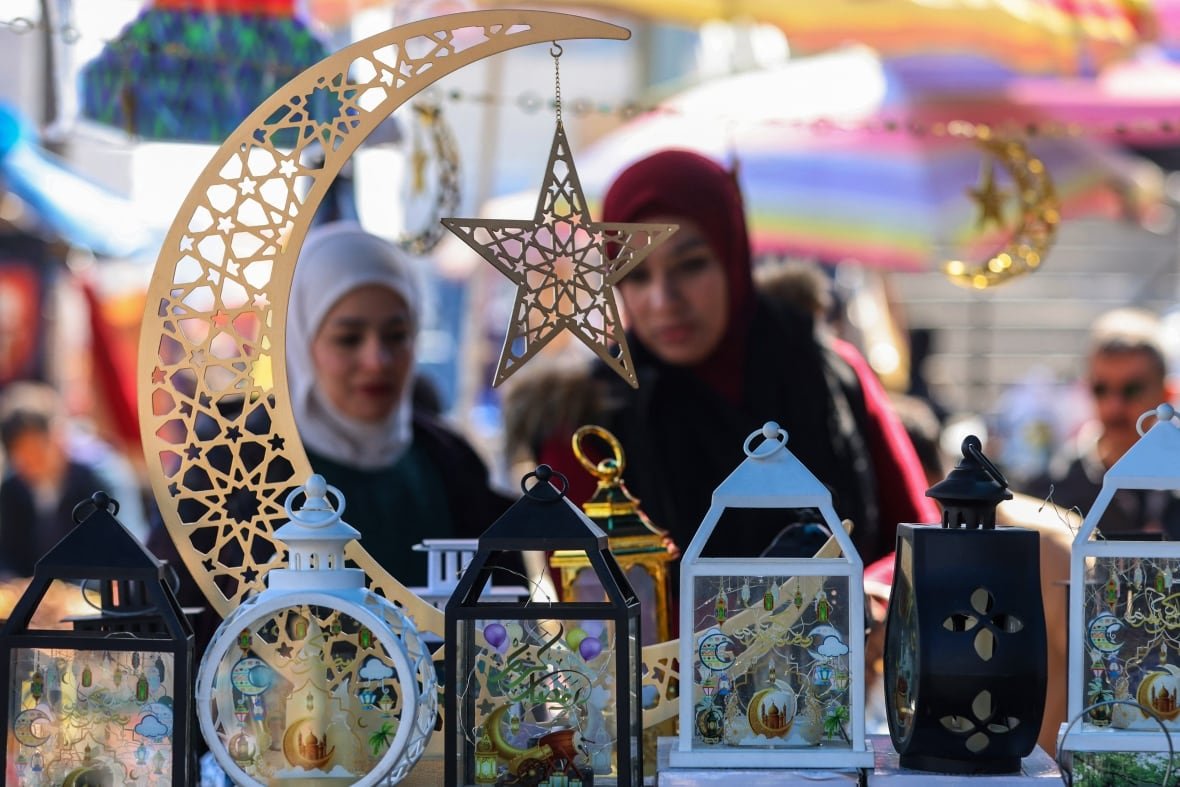 Women in headscarves shop for traditional lanterns at a market.