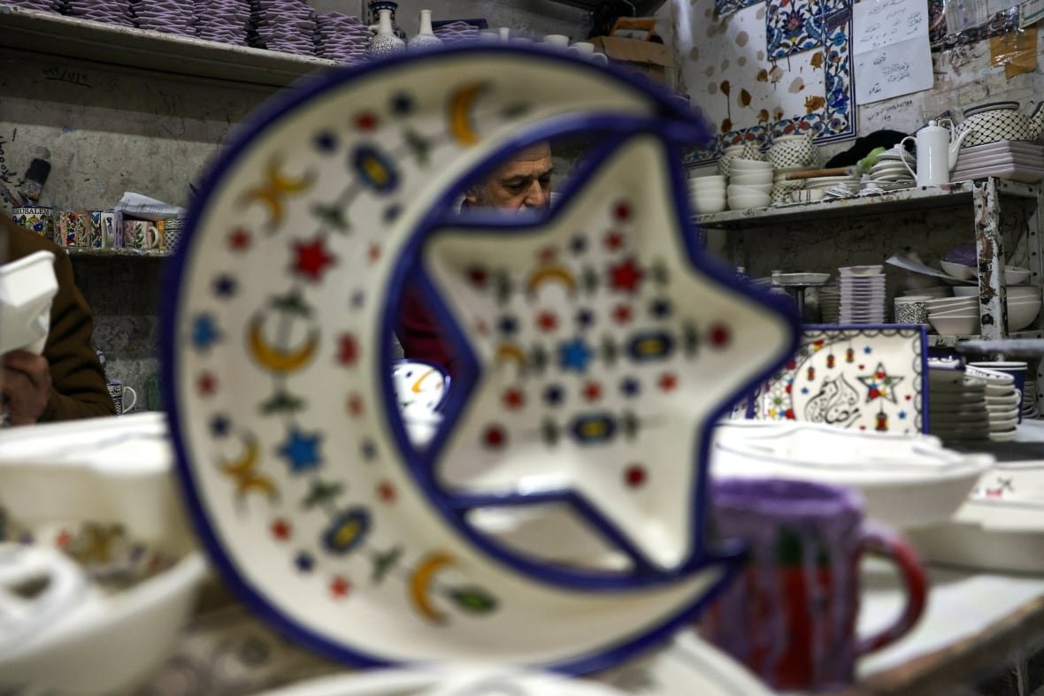 A man decorates ceramic plates ahead of Ramadan in his shop surrounded by wares.