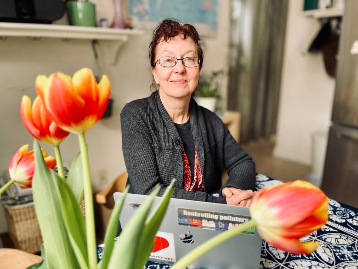 A woman sits in an indoor room, with a laptop computer open in front of her and red-and-yellow tulips in soft focus in the foreground.