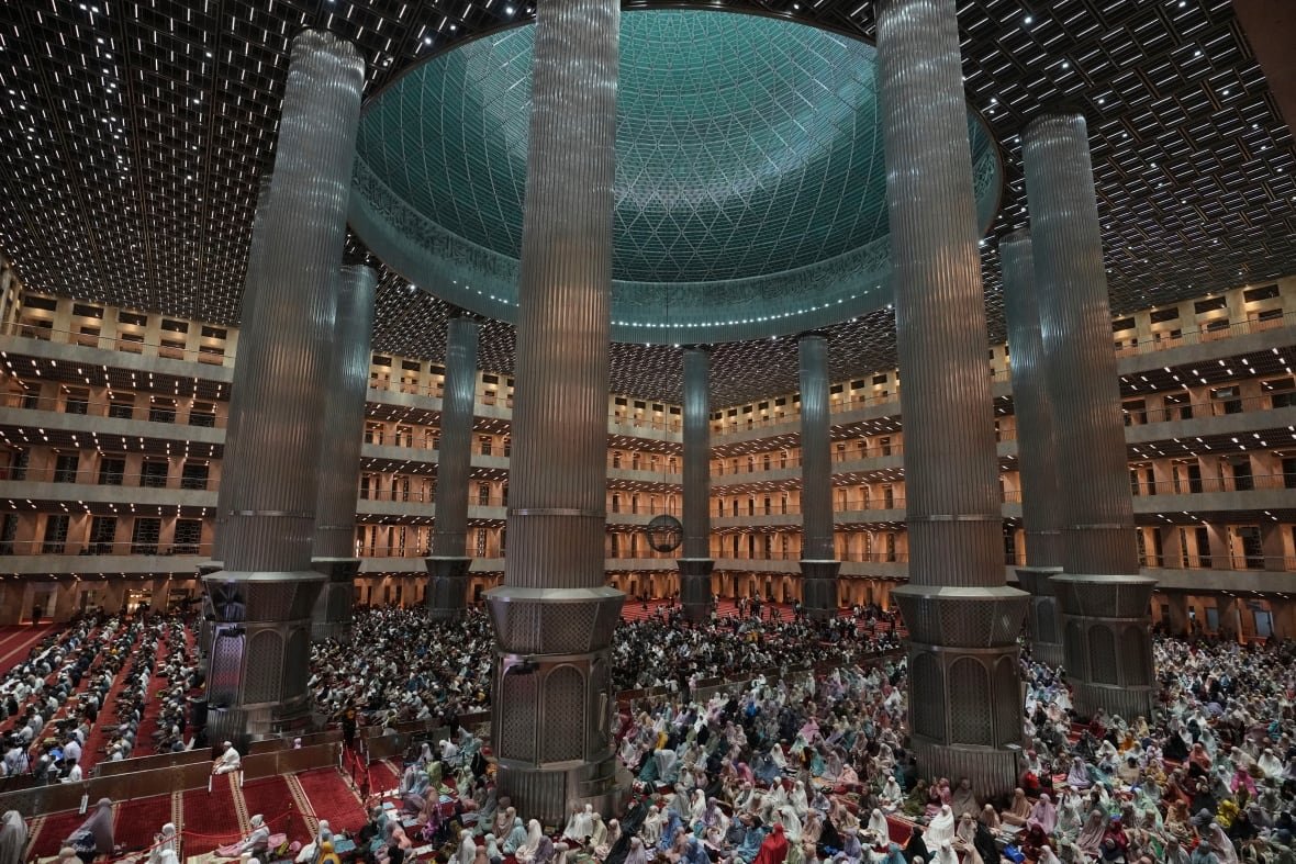 A wide shot of Muslims praying in a vast mosque.