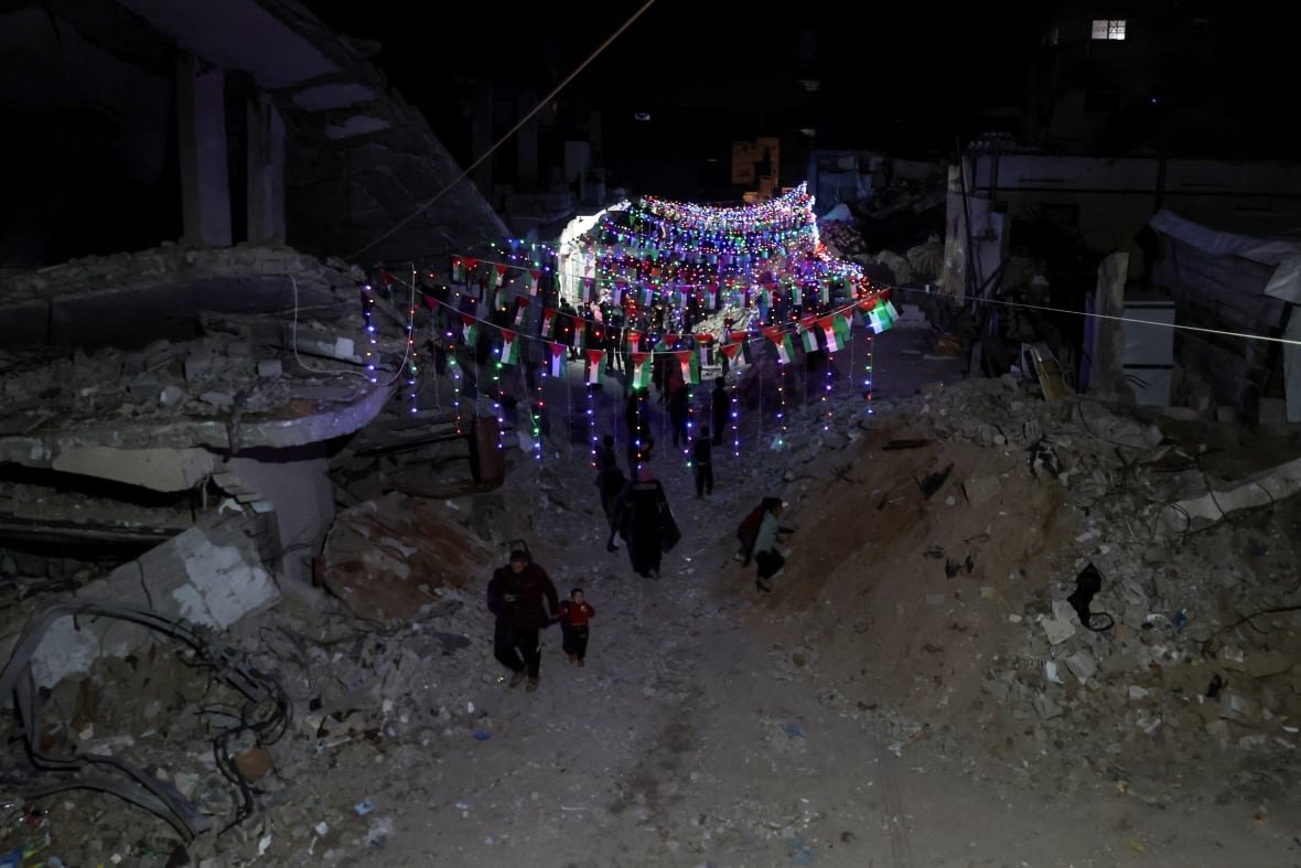 Palestinians walk under decorative lights strung up between the rubble of buildings, ahead of Ramadan