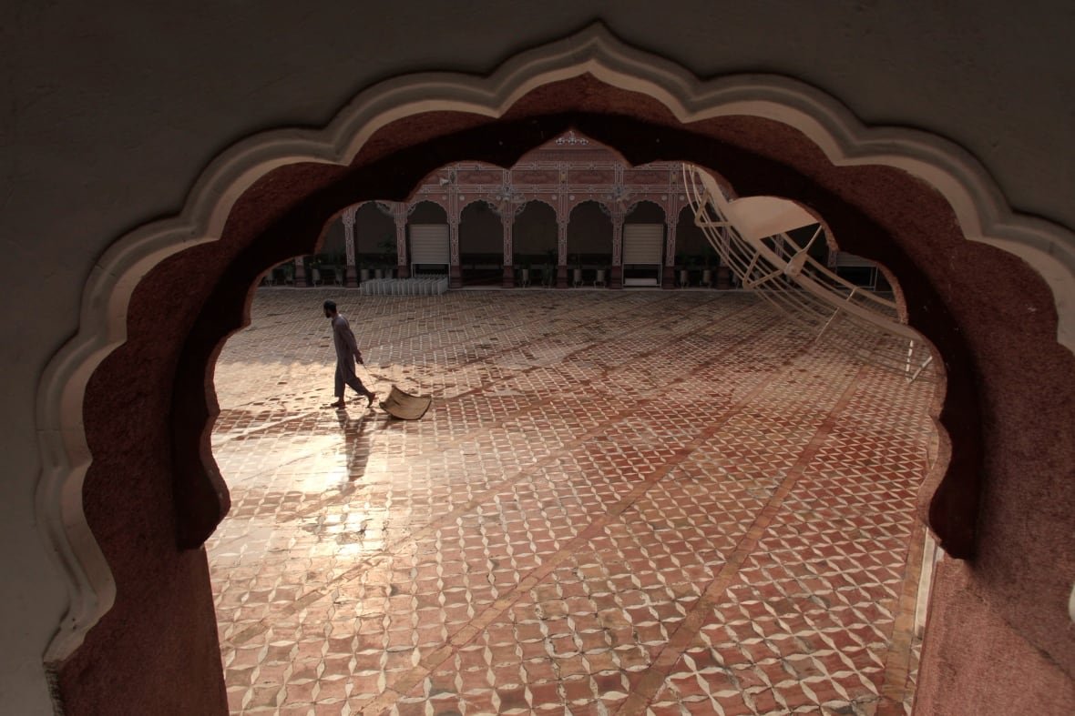 Framed by an archway, a worker cleans a historical mosque in preparation for Ramadan