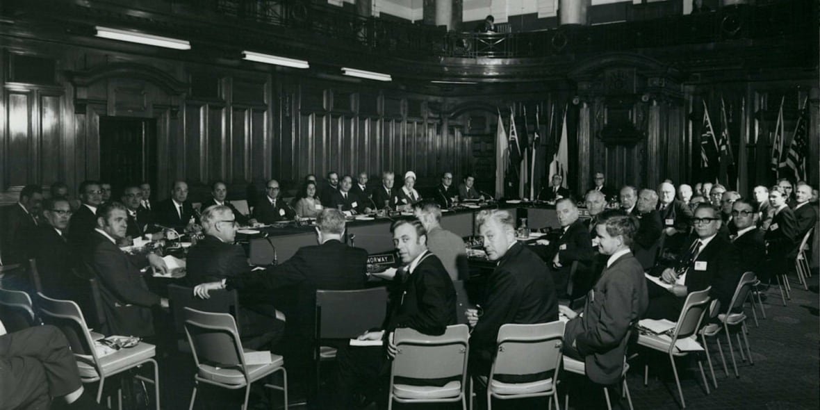 A black and white photo of a bunch of people in a large room.