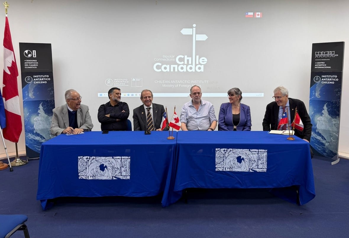 A bunch of people sit at a table with a sign reading 'Polar Connections Chile-Canada' in the background.