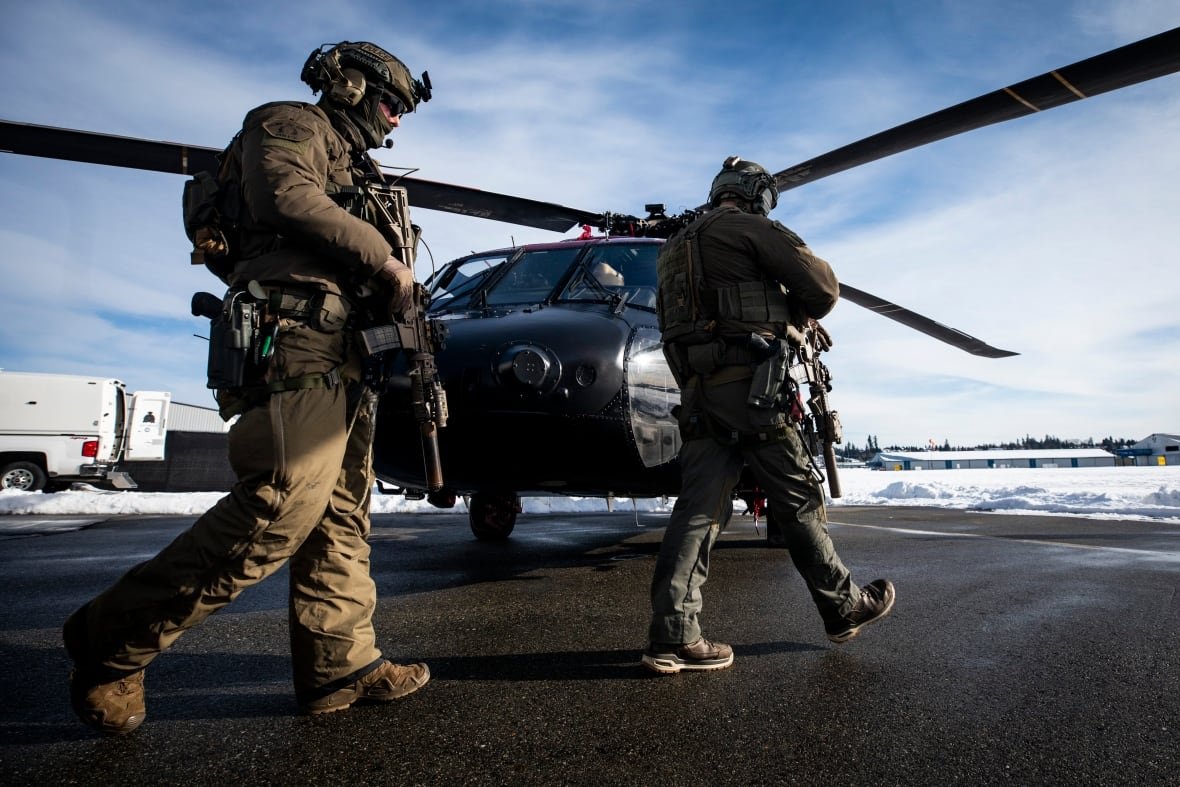 Two heavily-armed soldiers are seen walking towards a helicopter on a snowy day.