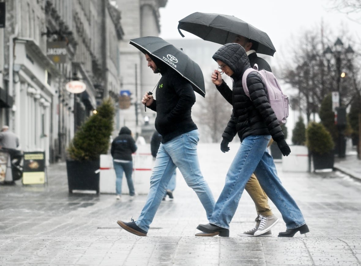 wea-spring-storm-20250330 People walk with umbrellas during rainfall.