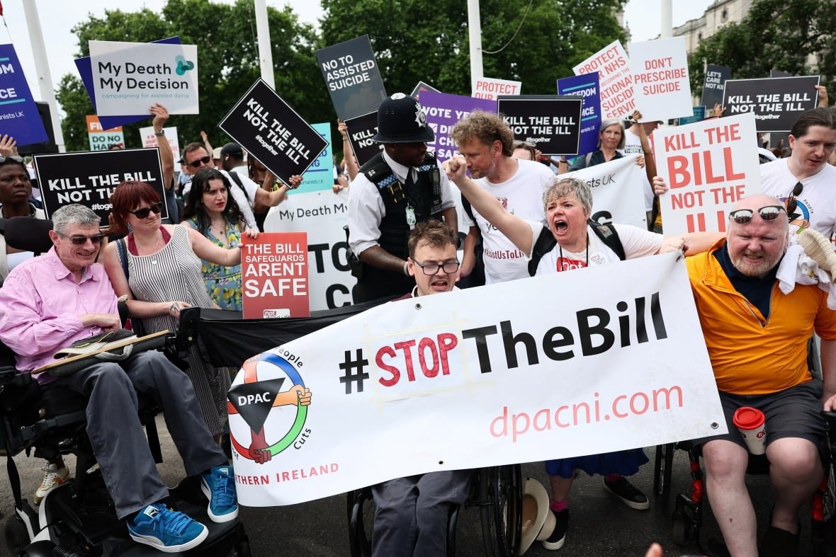 britain-assisted-dying Several people, including a few in wheelchairs, hold up placards and signs in an outdoor protest. Signs say 'Kill the Bill' or "Stop the Bill.'