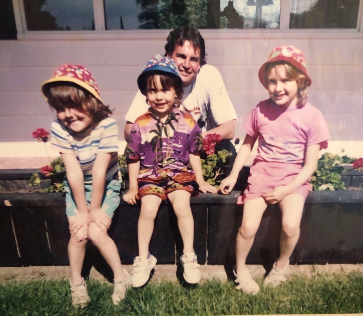 Three young kids in sunhats pose with their dad.