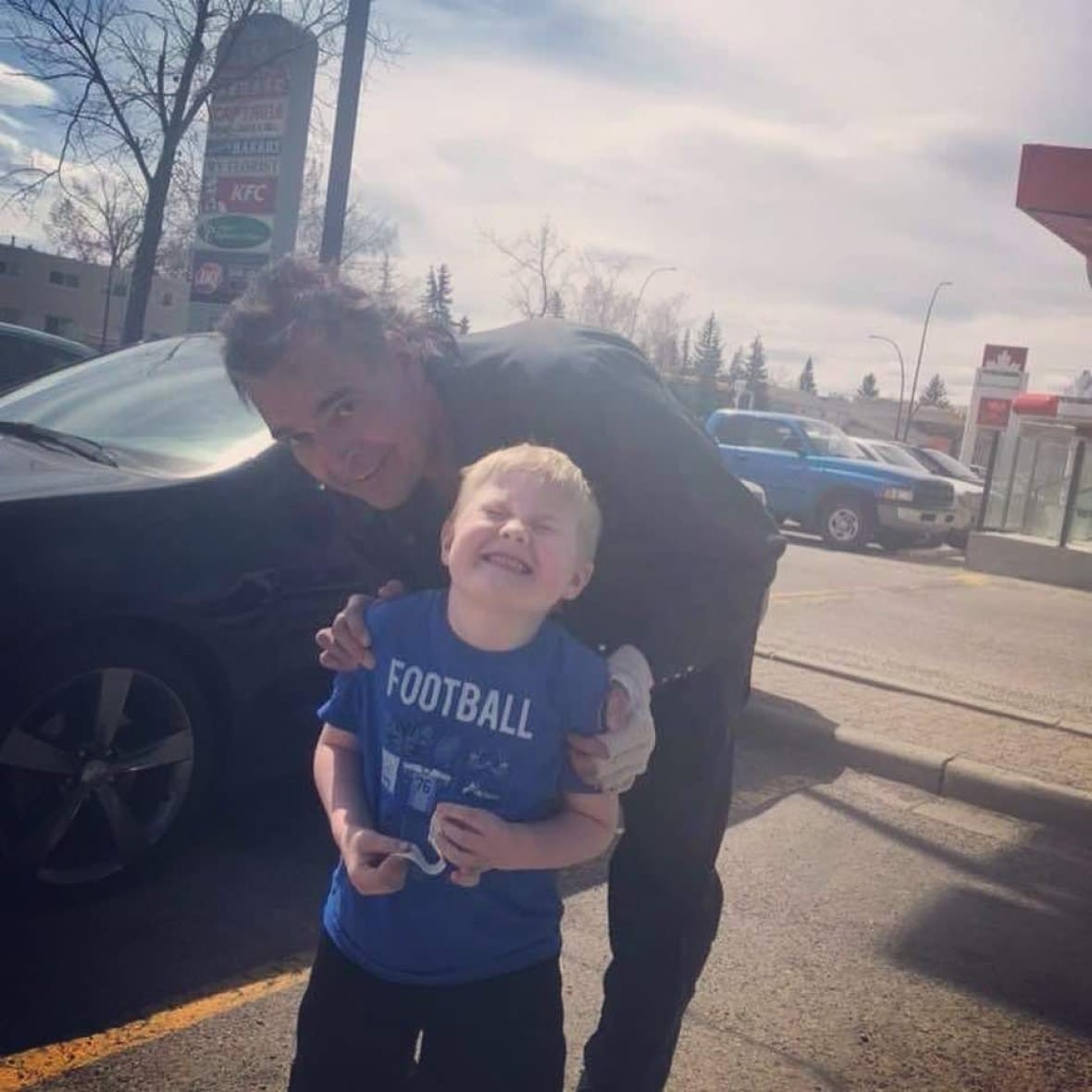 A man and a boy pose in a parking lot.