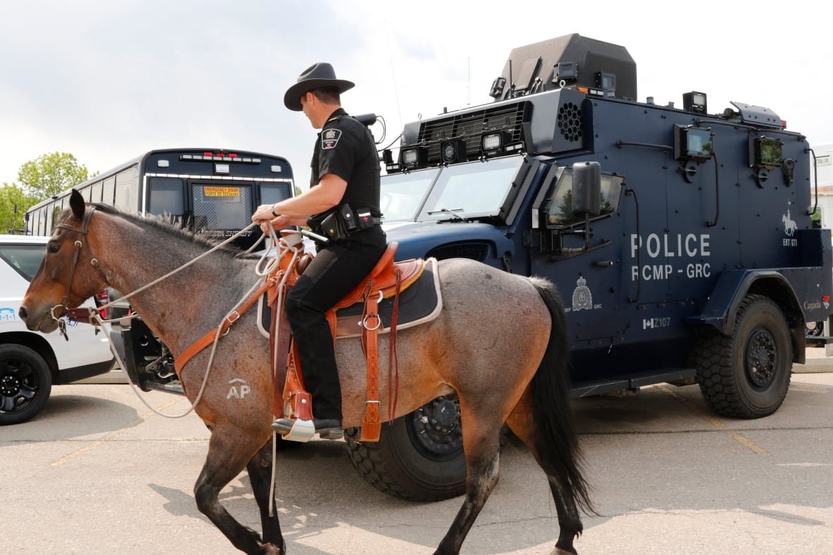 A police officer on horseback rides past a police vehicle.