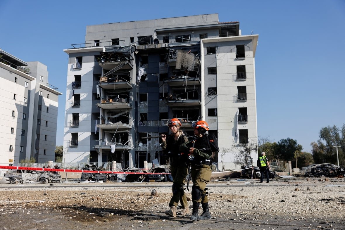 iran-nuclear-israel-3 Two people wearing orange helmets stand in front of a damaged residential building.