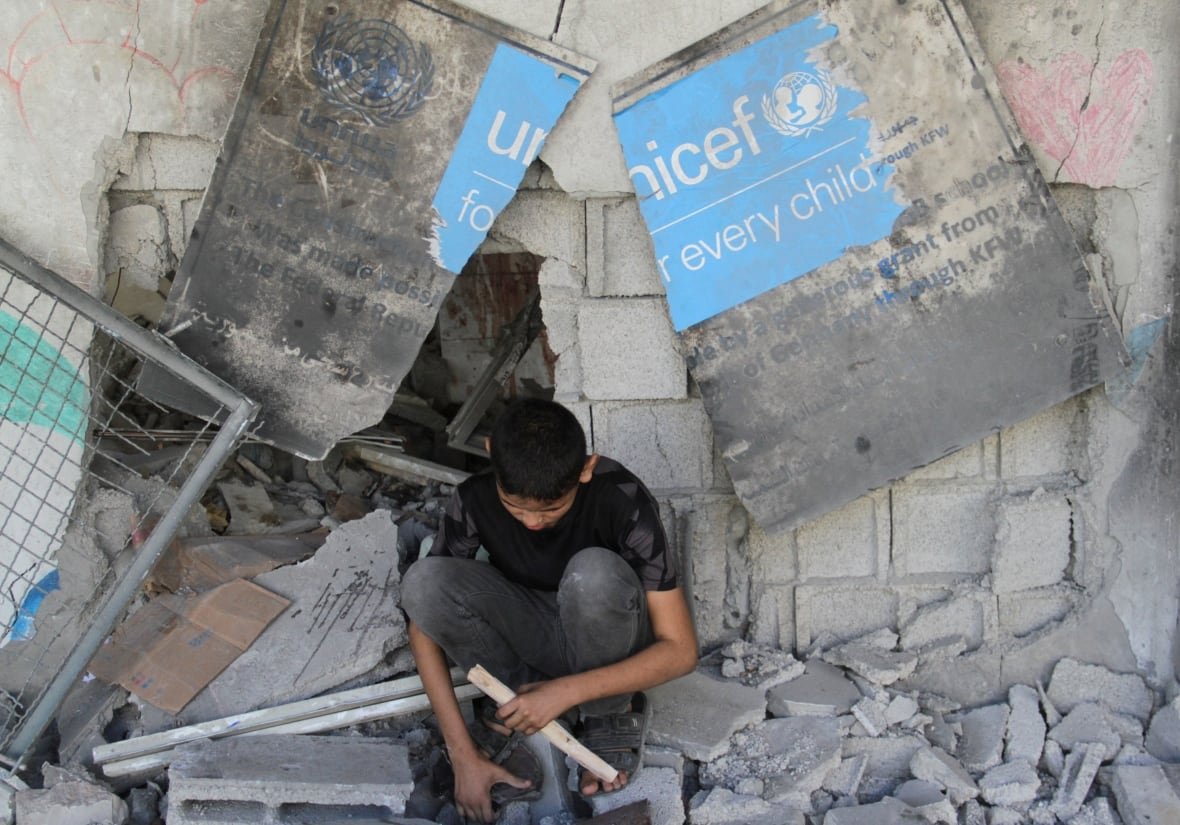 israel-palestinians-5 A boy sits under a broken UNICEF sign.
