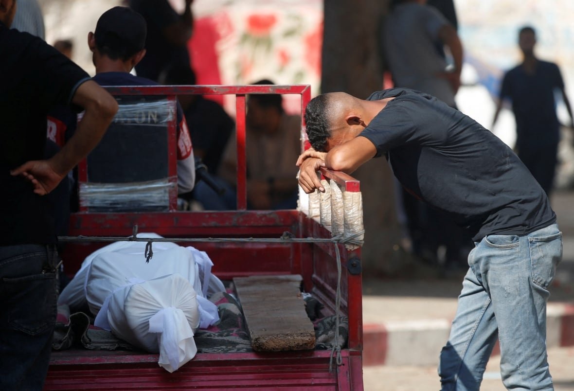 israel-palestinians-gaza-aid-2 A man puts his head down on a cart carrying a body of a person in white shroud.