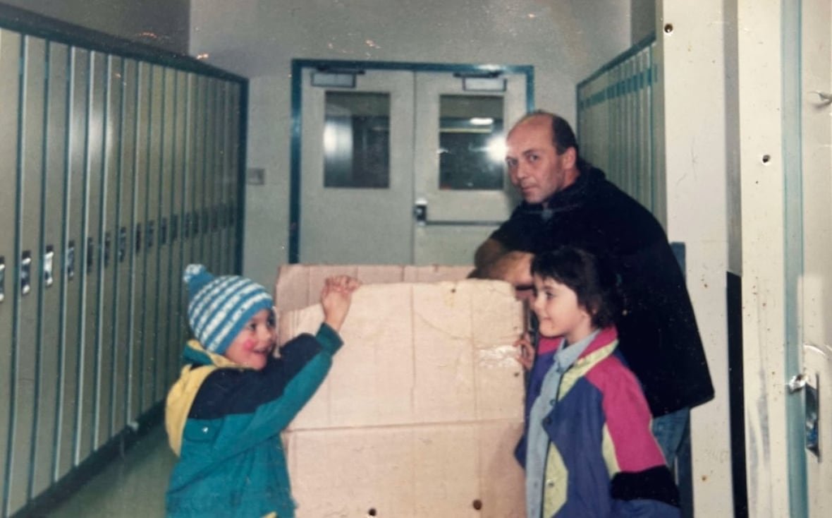An old photo of two kids in winter coats and a man in a school hallway.