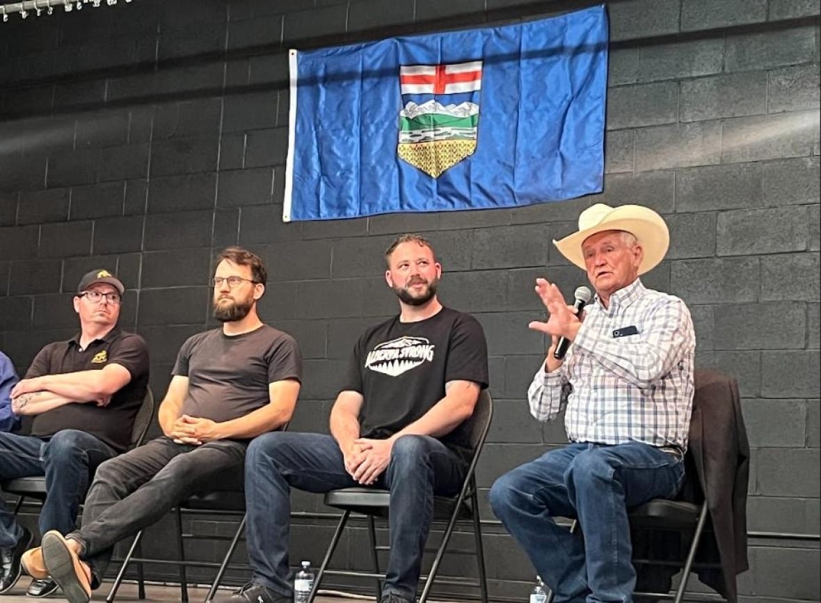 separatists four men sit, with an Alberta flag taped to the cinder block wall behind them
