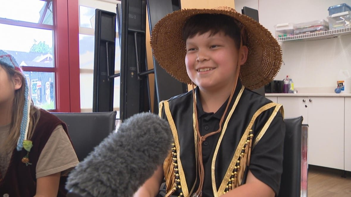 thomas-jacobs An Indigenous child wearing a hat smiles.