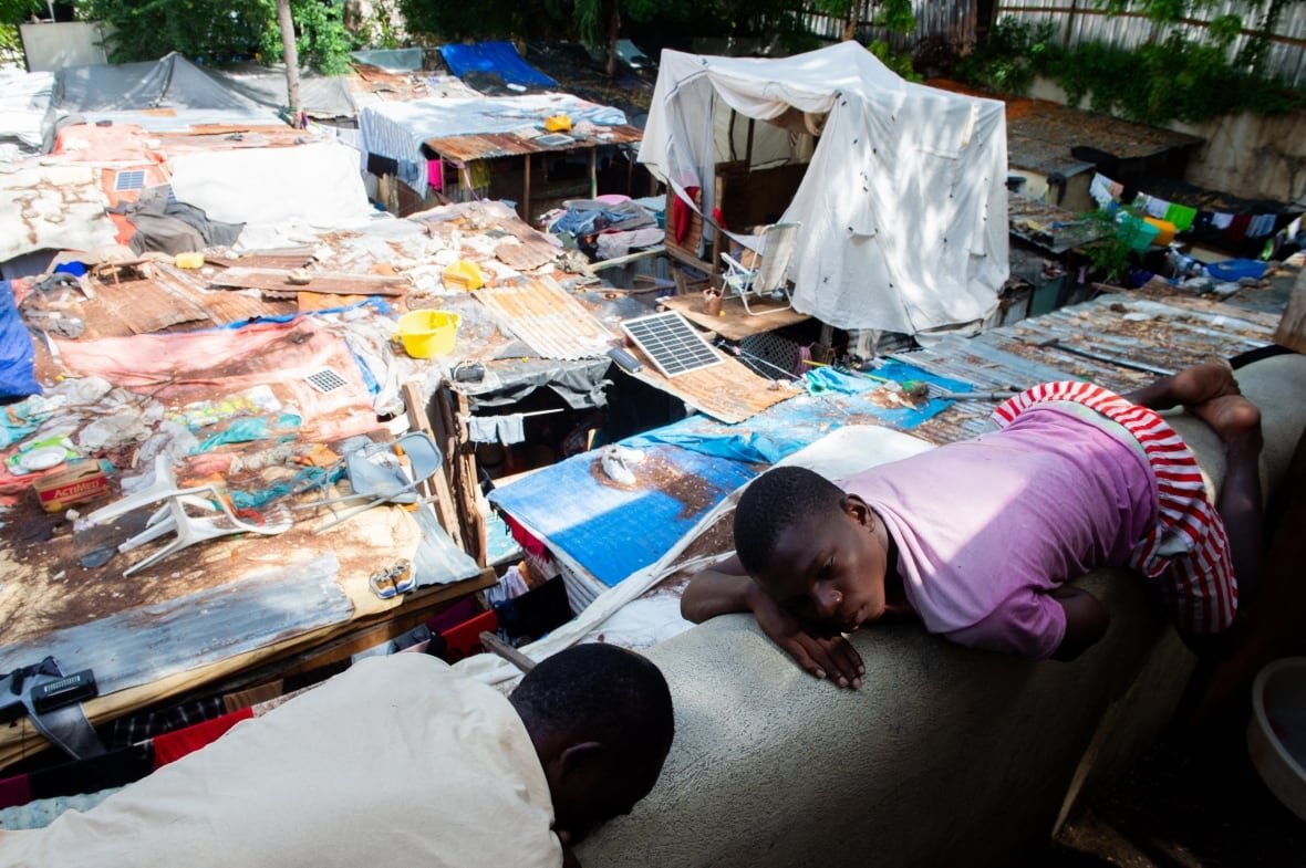 Two dark-complected people lie on the ground in a makeshift shelter.