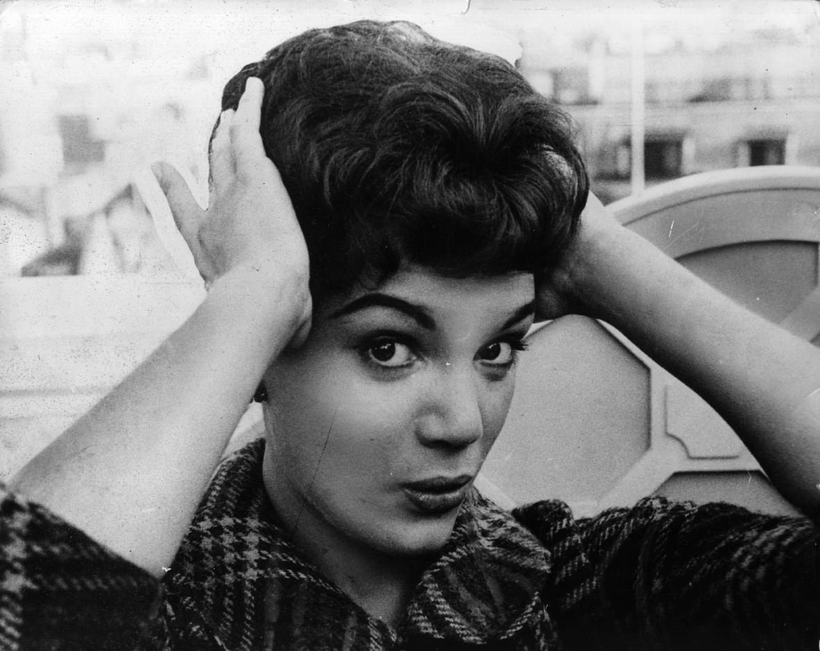3303878-connie-francis A black and white photo of a woman holding her short black hair while looking into the camera.