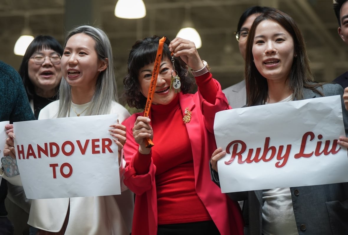 A group of people smile. Two of them are holding up signs reading 'handover to Ruby Liu'.
