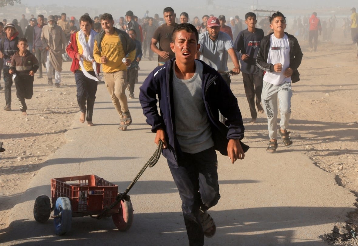 israel-palestinians-ghf A crowd of people run on a dusty sandy road