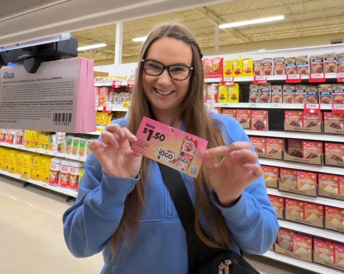 A woman holds up a coupon in the aisle of a  grocery store
