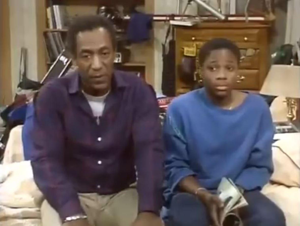 malcolm-jamal-warner-bill-cosby-the-cosby-show A man sits on a bed next to a teenage boy.