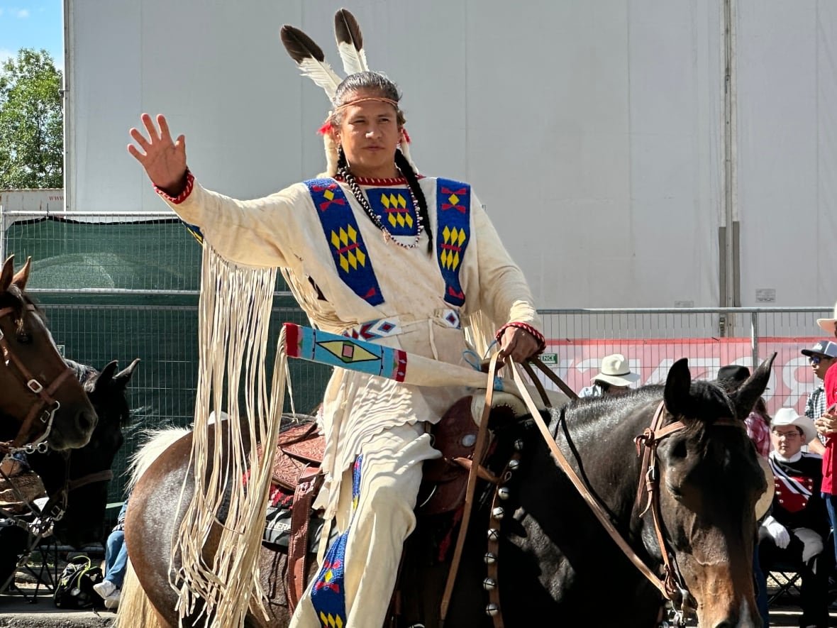 Person wearing First Nation regalia on horse.