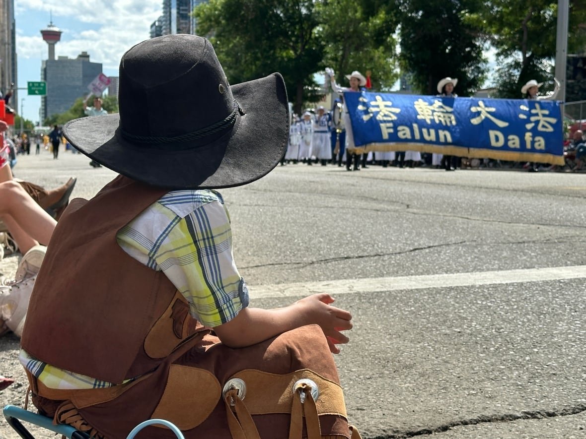 A boy in western wear sits on the curb and waits for the next group, Falun Dafa, to make its way down the road.