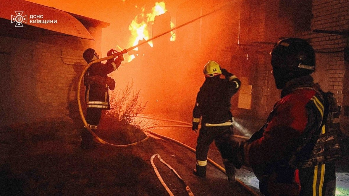 russia-ukraine-war A video still shows firefighters in uniform during nighttime hours using a hose as flames are shown coming from a building.