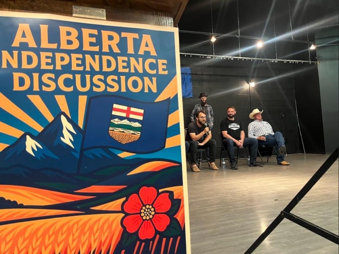 three-hills-independence a big sign for Alberta independence in foreground, seated speakers in background