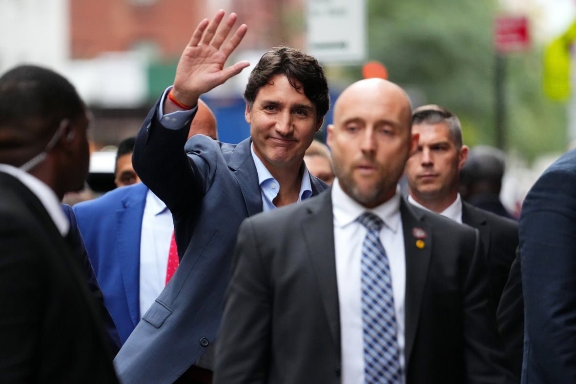 trudeau-colbert-20240923 A clean-shaven darkhaired man in a suit and collared shirt waves in an outdoor photo.