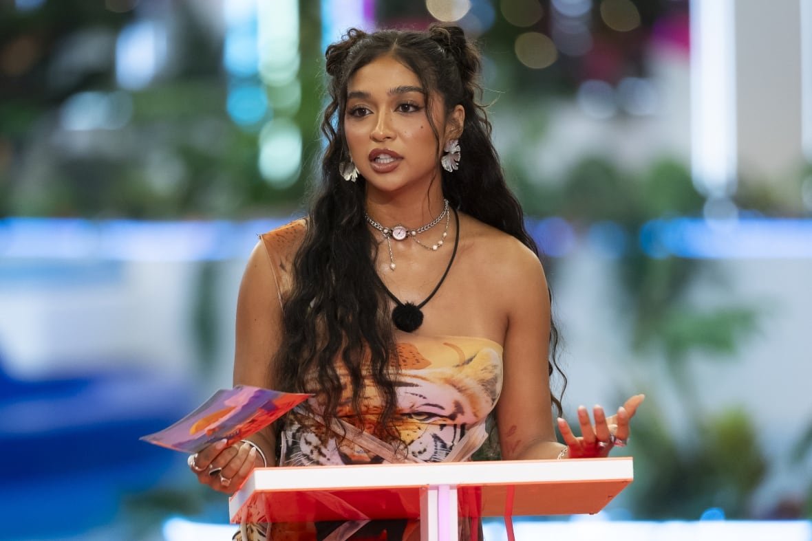 tv-love-island-cierra-ortega-apology A woman with long, brown, curly hair stands at a podium with a speech cards in her right hand.