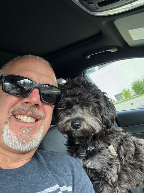 default-334 A smiling man takes a selfie with a black dog.