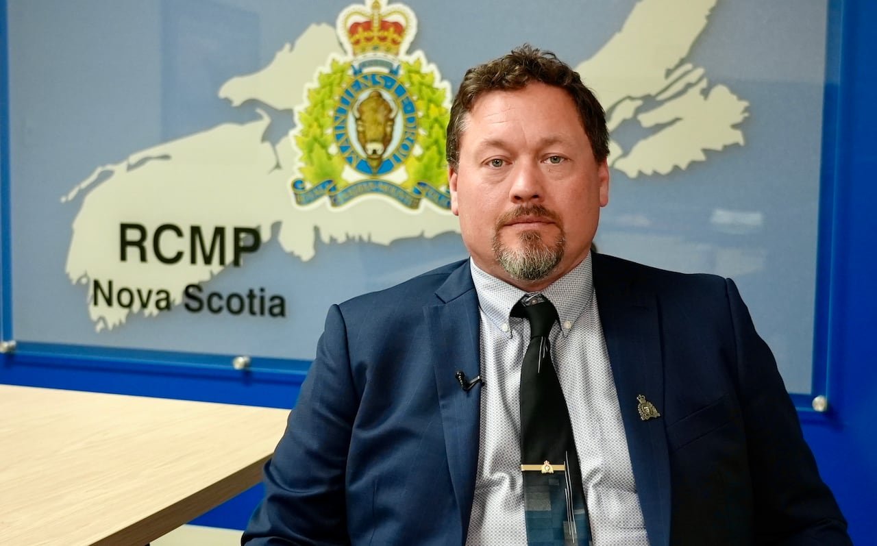 Man in blue suit sits in front of a map of Nova Scotia.