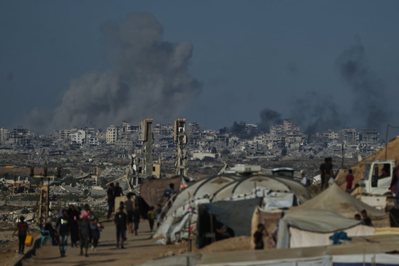 Smoke rises in a dark sky above buildings and tents