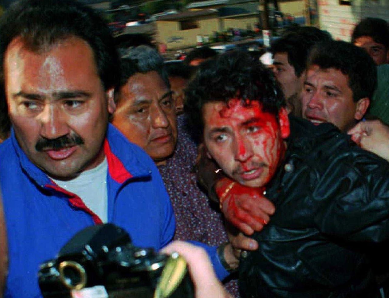 A man with his face bloodied is grabbed and pulled by a group of other men.